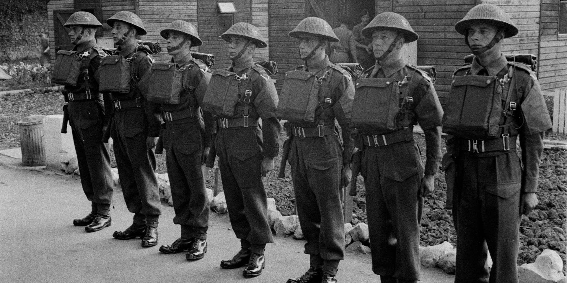 A parade of soldiers in helmets, gas mask cases on their chests and holstered revolvers at their sides